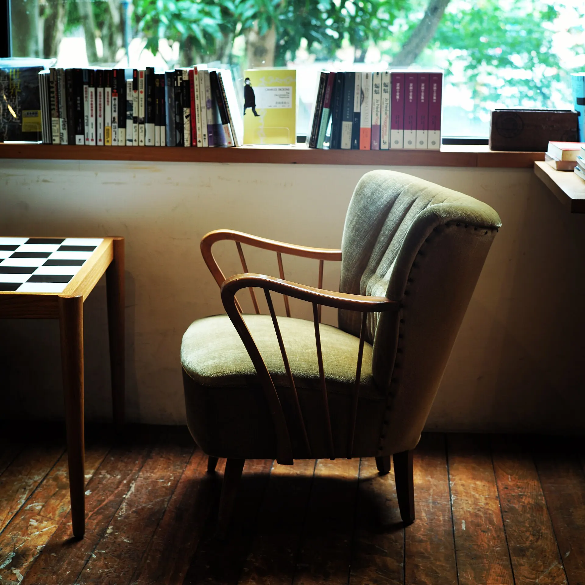 A green upholstered armchair with a wooden frame by a bookshelf