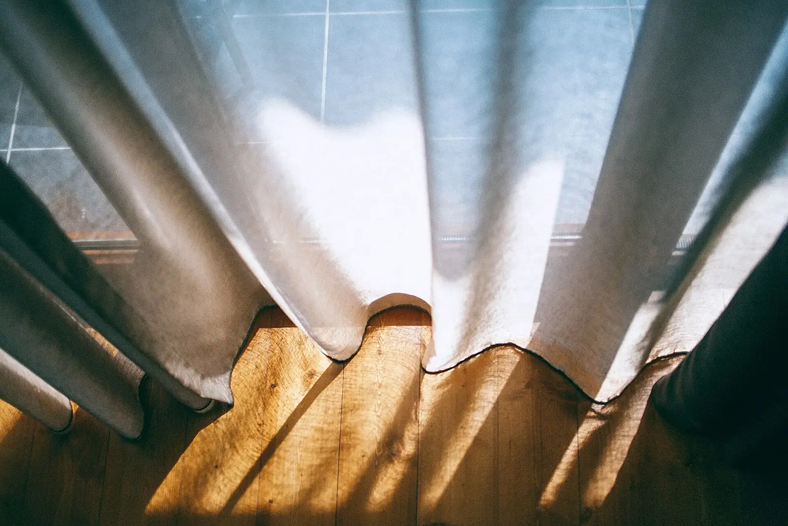 Heavy cream curtains falling to a sunlit wooden floor