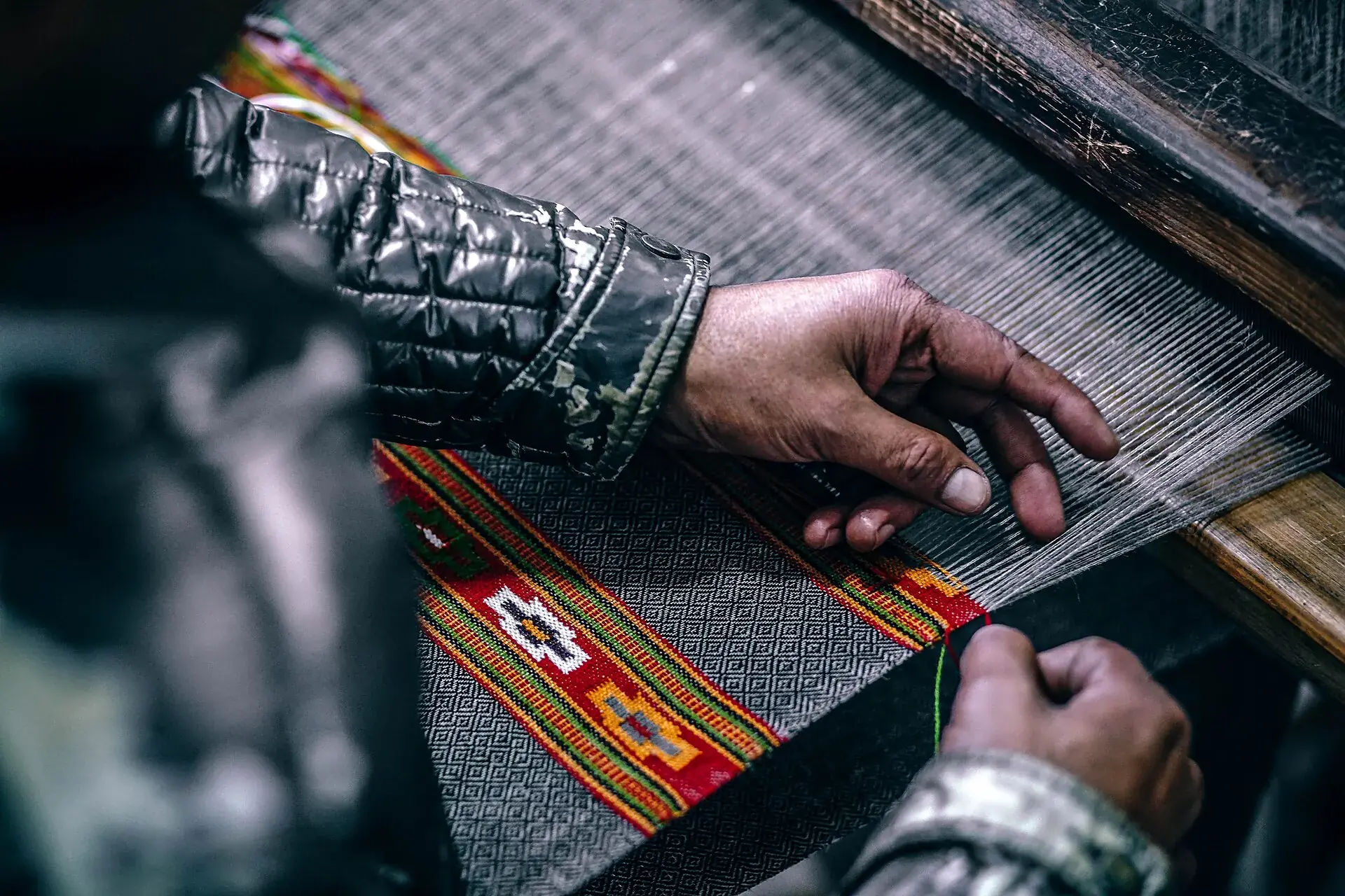 A weaver's hands passing the weft through a hand loom with a red and gold border